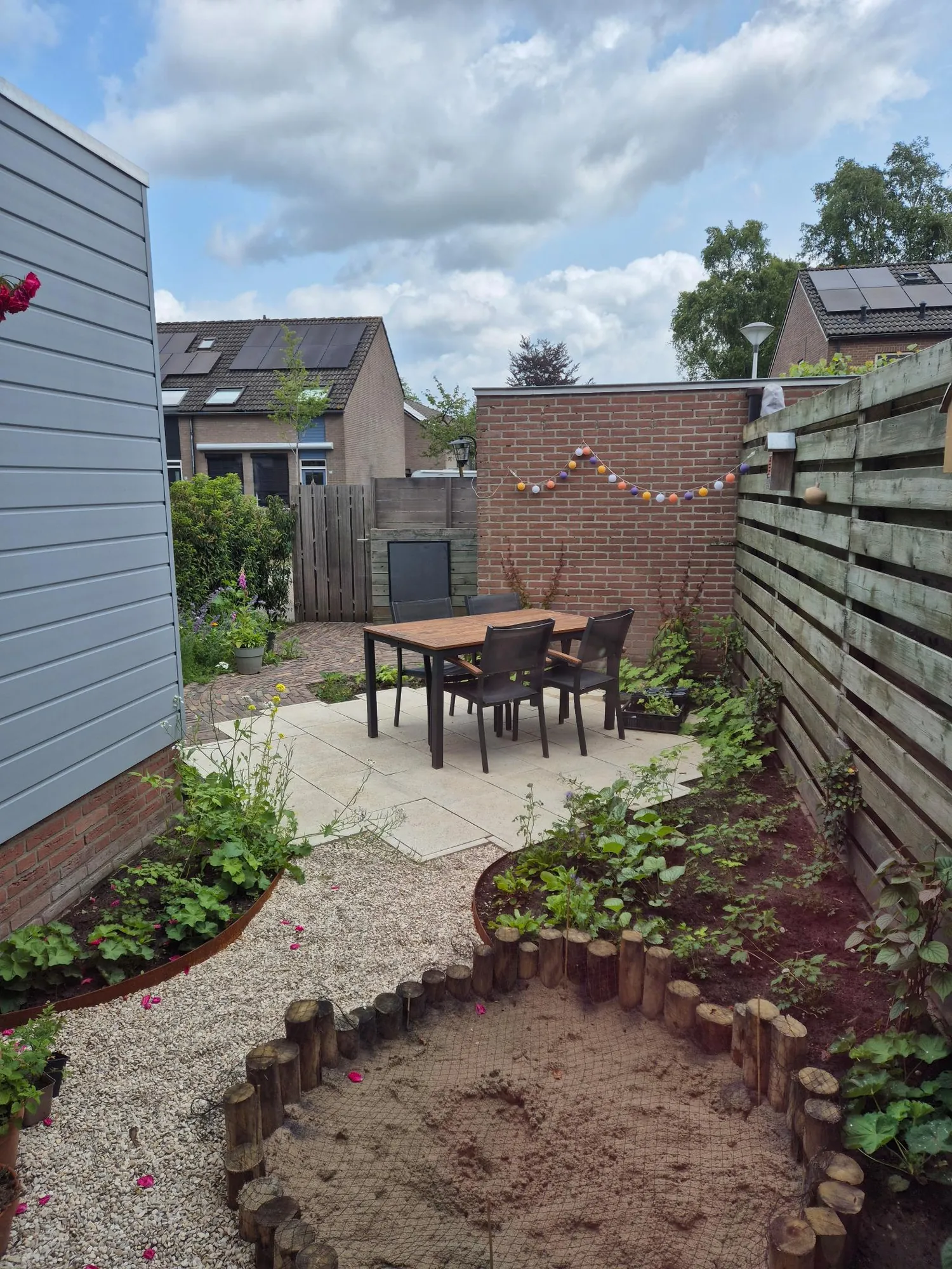 Achtertuin in Warnsveld met een zandbak van kastanjehout, terras en jonge borders