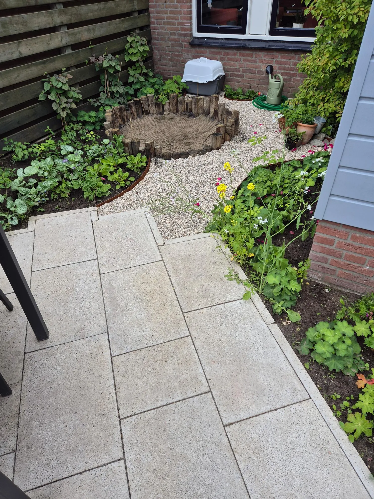 Terras met lichte tegels, grindpad en ronde zandbak in een tuin in Warnsveld