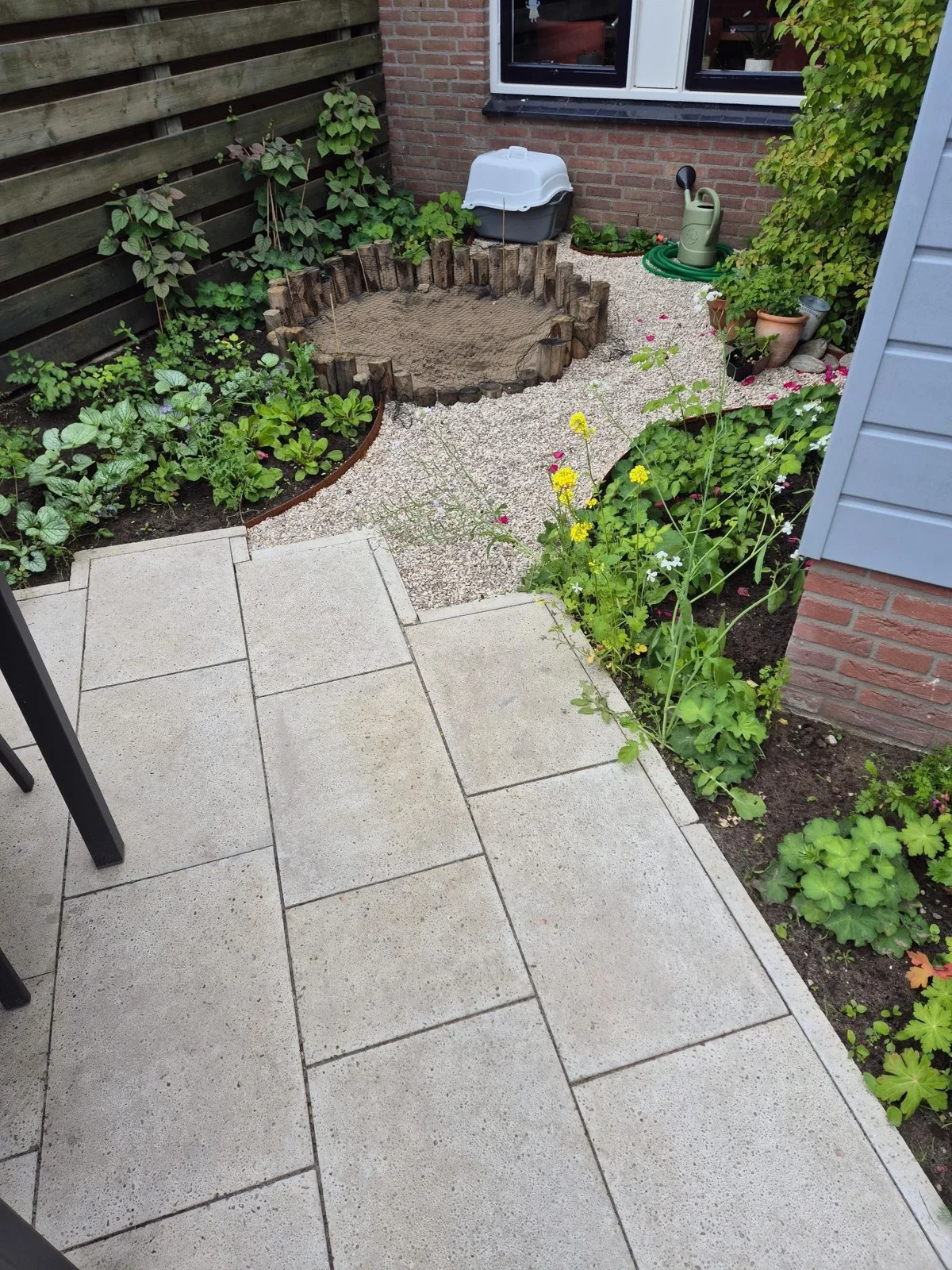 Terras met lichte tegels, grindpad en ronde zandbak in een tuin in Warnsveld
