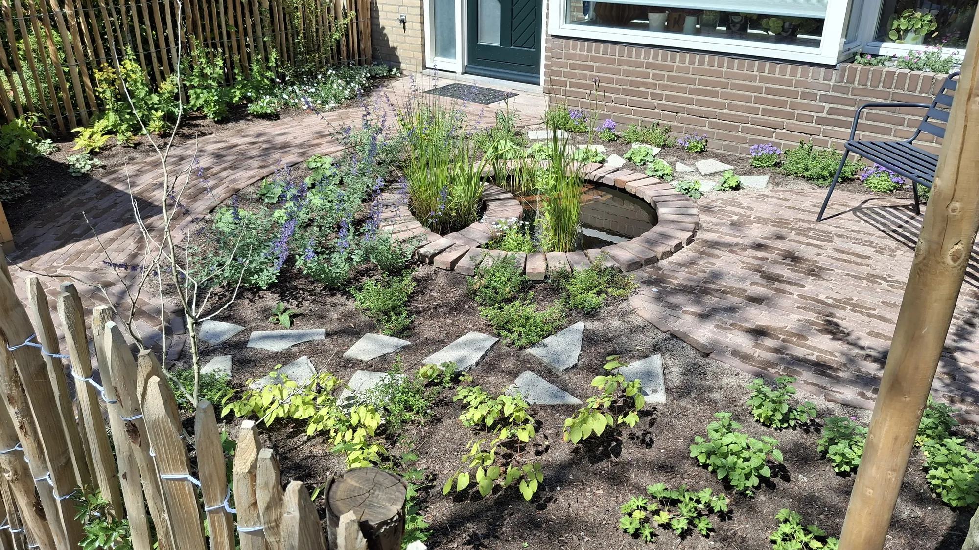 Voortuin in De Bilt met een ronde vijver, stapstenen en jonge borders achter een kastanjehouten hek