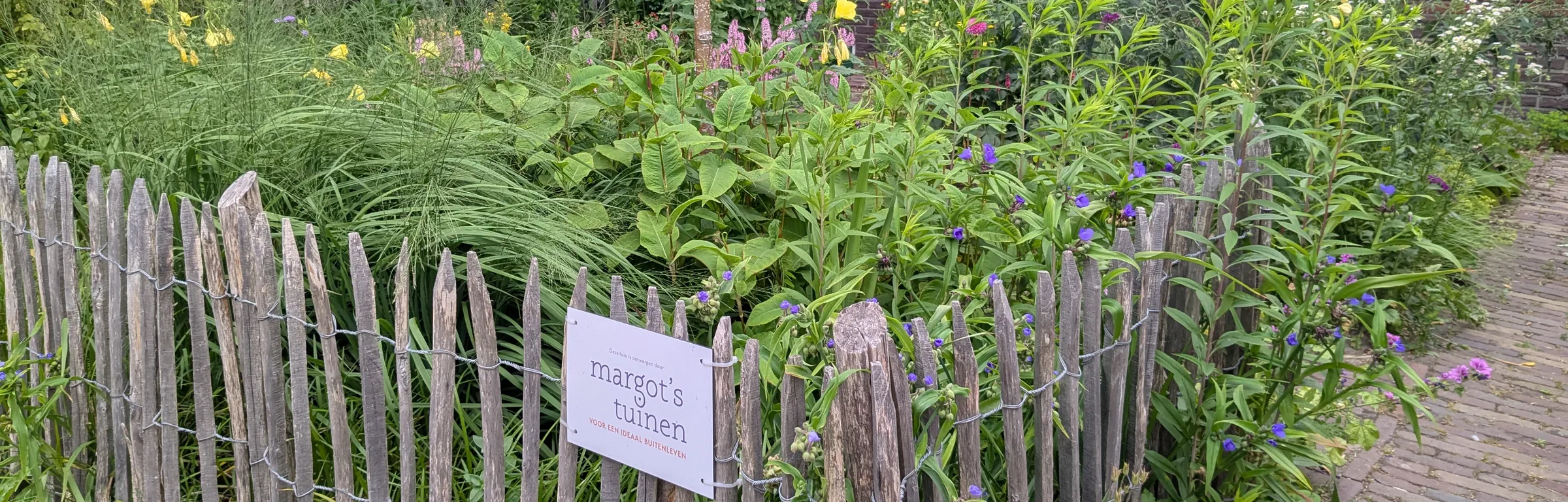 Kastanjehouten hek met het bordje van Margot's Tuinen voor een bloeiende tuin in De Bilt